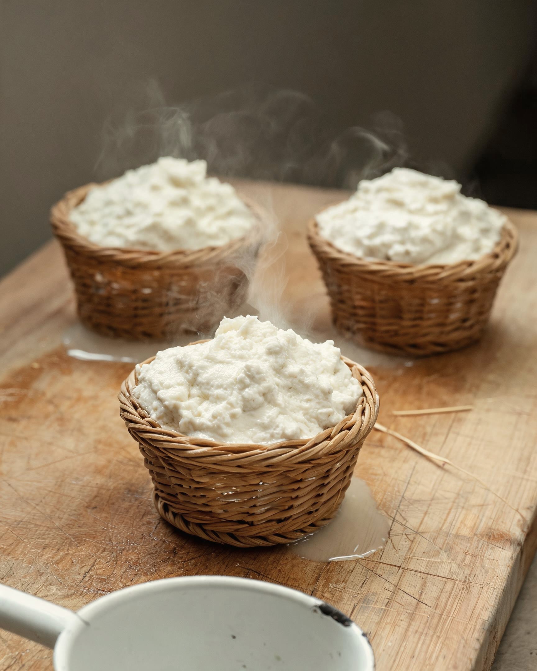 Warm ricotta steaming in three small woven baskets on a wooden board