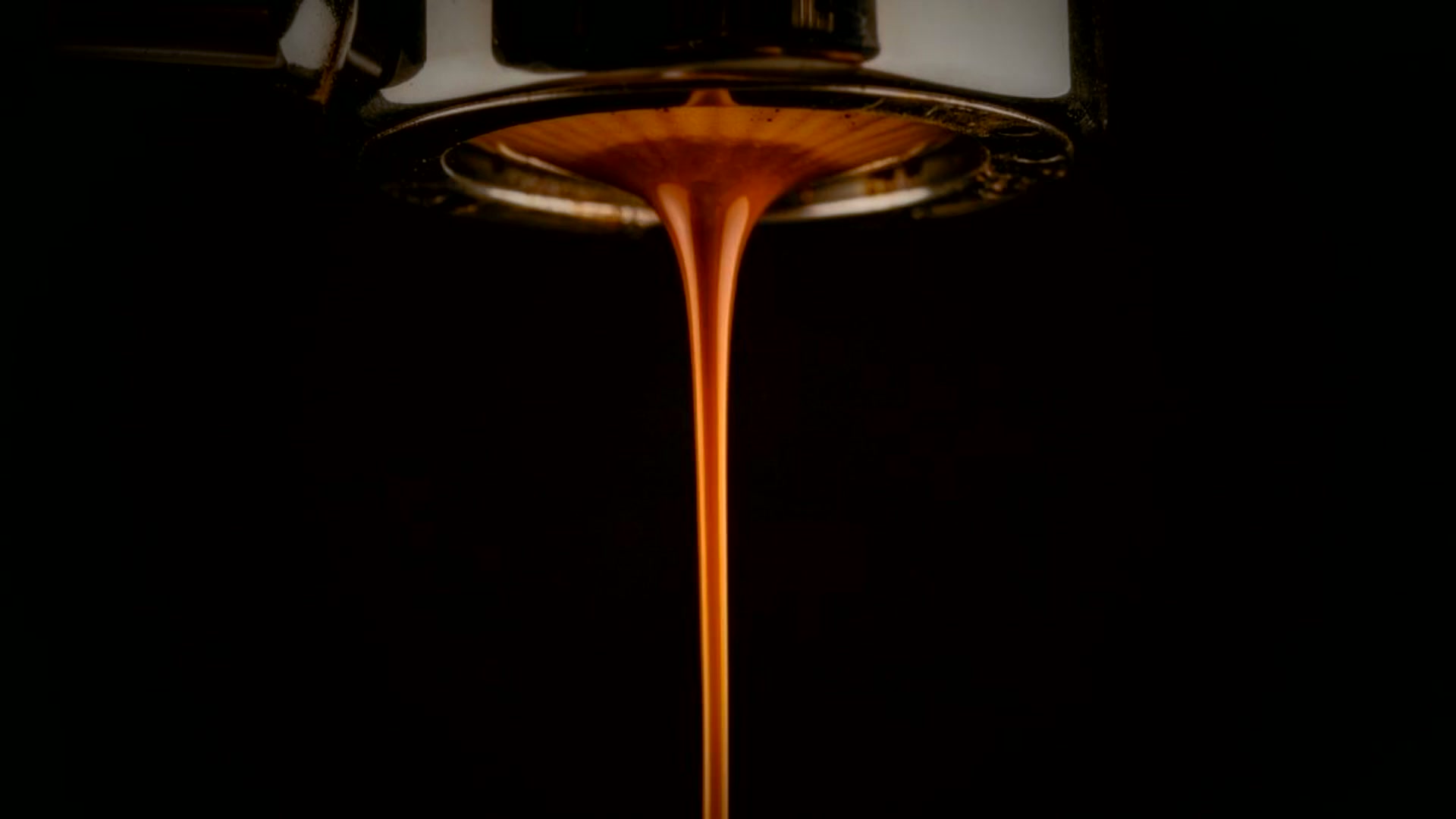 Espresso falling from a bottomless portafilter in near darkness.