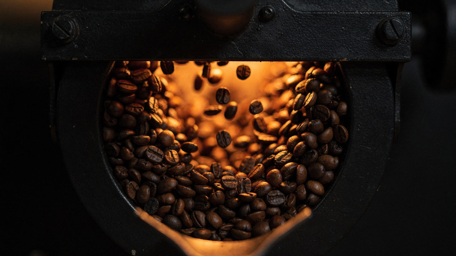 Coffee beans turning inside a roaster drum, lit from within.
