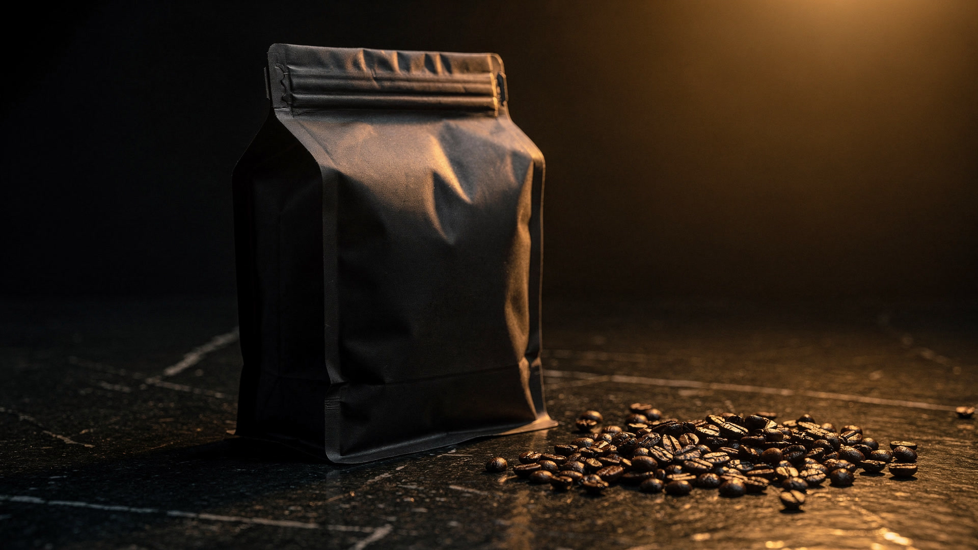A sealed dark coffee bag on stone with roasted beans beside it.